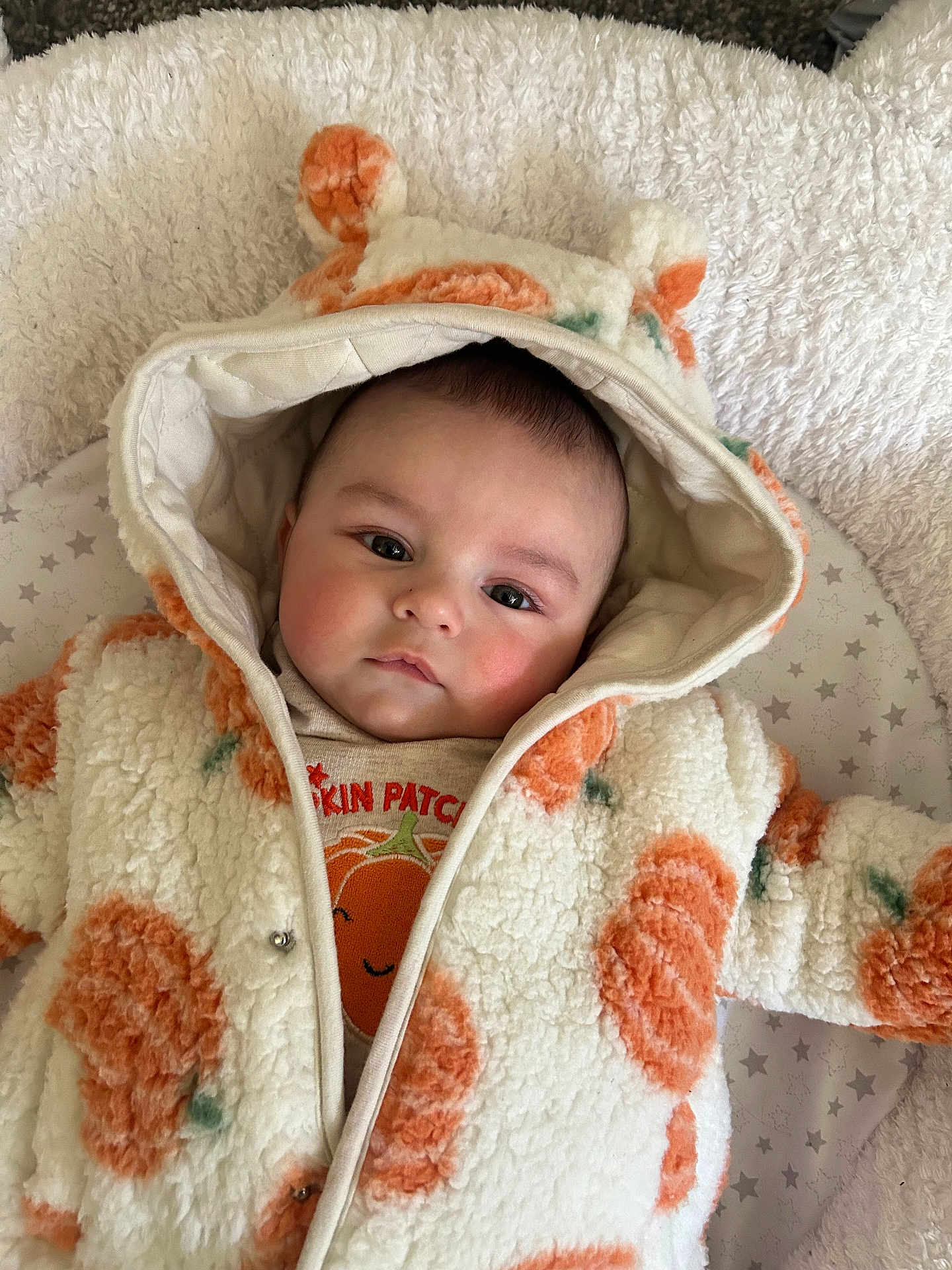 Albie is registered to the contest to win money with this photo: baby, infant, hooded_jacket, orange_flower_pattern, blanket, soft_texture, face, cute, portrait, lying_down, child, warm_clothing, star_pattern, indoor, closeup, young_child, expression, cozy, adorable, toddler