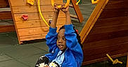 Tamar is registered to the contest to win money with this photo: child, playground, indoor, play_equipment, climbing_wall, slide, rings, yellow, blue_jacket, floral_pants, socks, fun, active, play, young, person, hands, smiling, rope, floor_mats