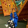 child, playground, indoor, play_equipment, climbing_wall, slide, rings, yellow, blue_jacket, floral_pants, socks, fun, active, play, young, person, hands, smiling, rope, floor_mats