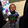 Kymani joined the competition — help win amazing prizes! child, boy, outdoor, sidewalk, car_door, table, cup, shirt, shorts, shoes, fence, sunlight, concrete, grass, party_tablecloth, food_container, holding_object, smiling, person, daytime