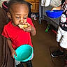 Kymani is registered to the contest to win money with this photo: toddler, child, indoor, red_shirt, blue_bowl, bread, eating, standing, playpen, wooden_drawers, floor, shoes, shorts, person, furniture, home, casual, snack, holding, young_child