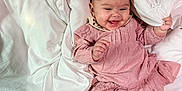 Stella is registered to the contest to win money with this photo: baby, infant, smile, pink_dress, headband, blanket, comforter, bed, happy, child, cute, legs, socks, indoor, person, portrait, young_child, cozy, fabric, toddler