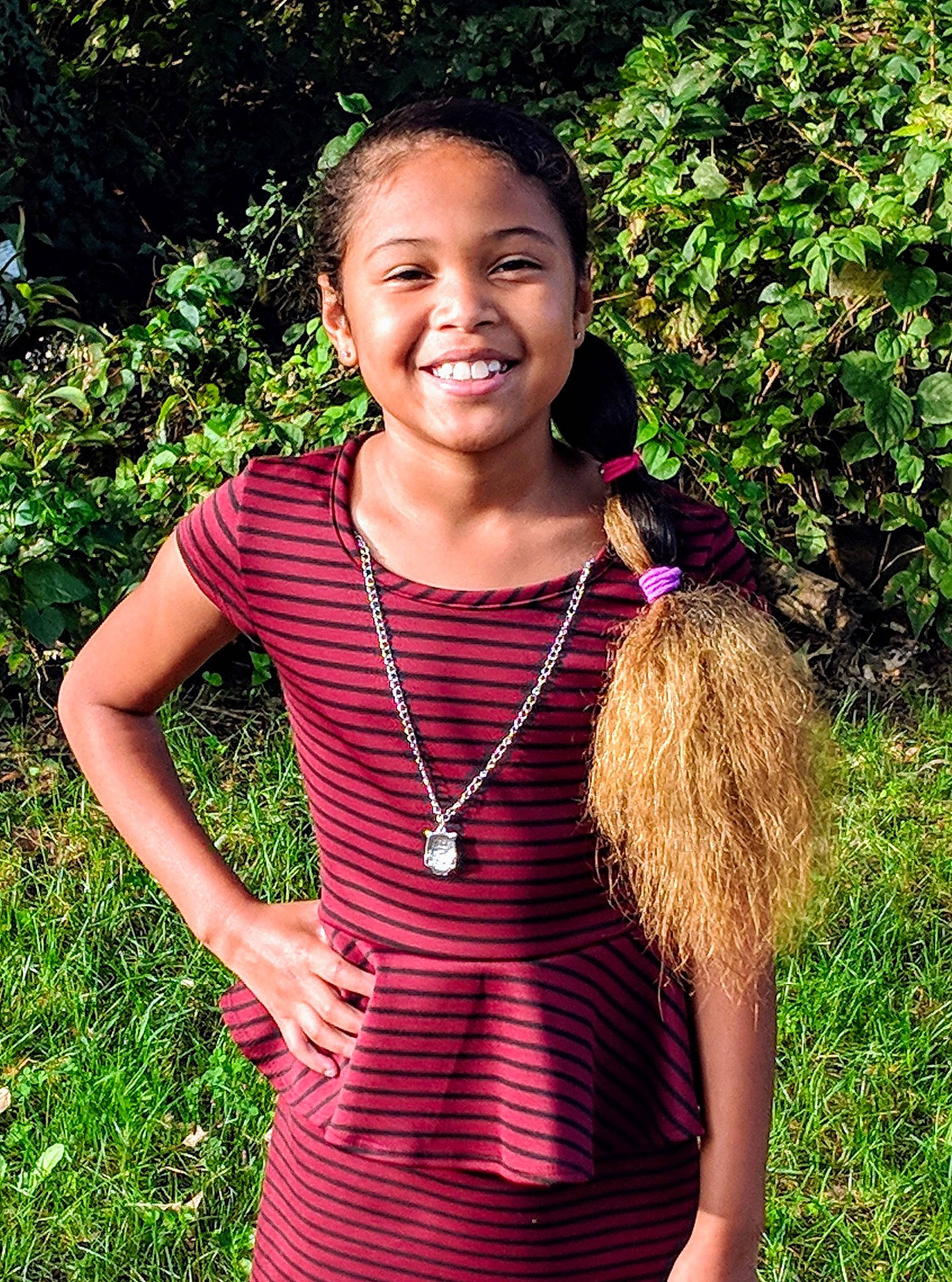 Yasmin is registered to the contest to win money with this photo: abdomen, child, child_model, clothing, emotion, facial_expression, fun, garden, girl, grass, grass_family, happiness, joy, long_hair, pattern, person, pink, plant, smile, tree