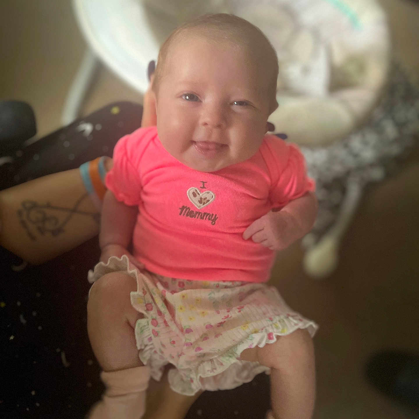 Haven is registered to the contest to win money with this photo: baby, baby_rocker, blurred_background, child, clothing, cute, face, happy, holding, indoor, infant, person, pink_shirt, portrait, skirt, small_person, smiling, socks, tattoos, tongue_out