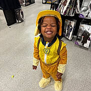 John Jr. is registered to the contest to win money with this photo: child, costume, yellow, helmet, smile, store, aisle, floor, halloween, packaging, clothing, young, happy, indoor, person, toy, pretend, fun, cute, shopping