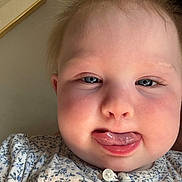 Rhea is registered to the contest to win money with this photo: baby, child, face, tongue, expression, close_up, cheeks, clothing, patterned_shirt, blue_eyes, skin, hair, button, indoors, portrait, person, cute, funny, infant, young_child