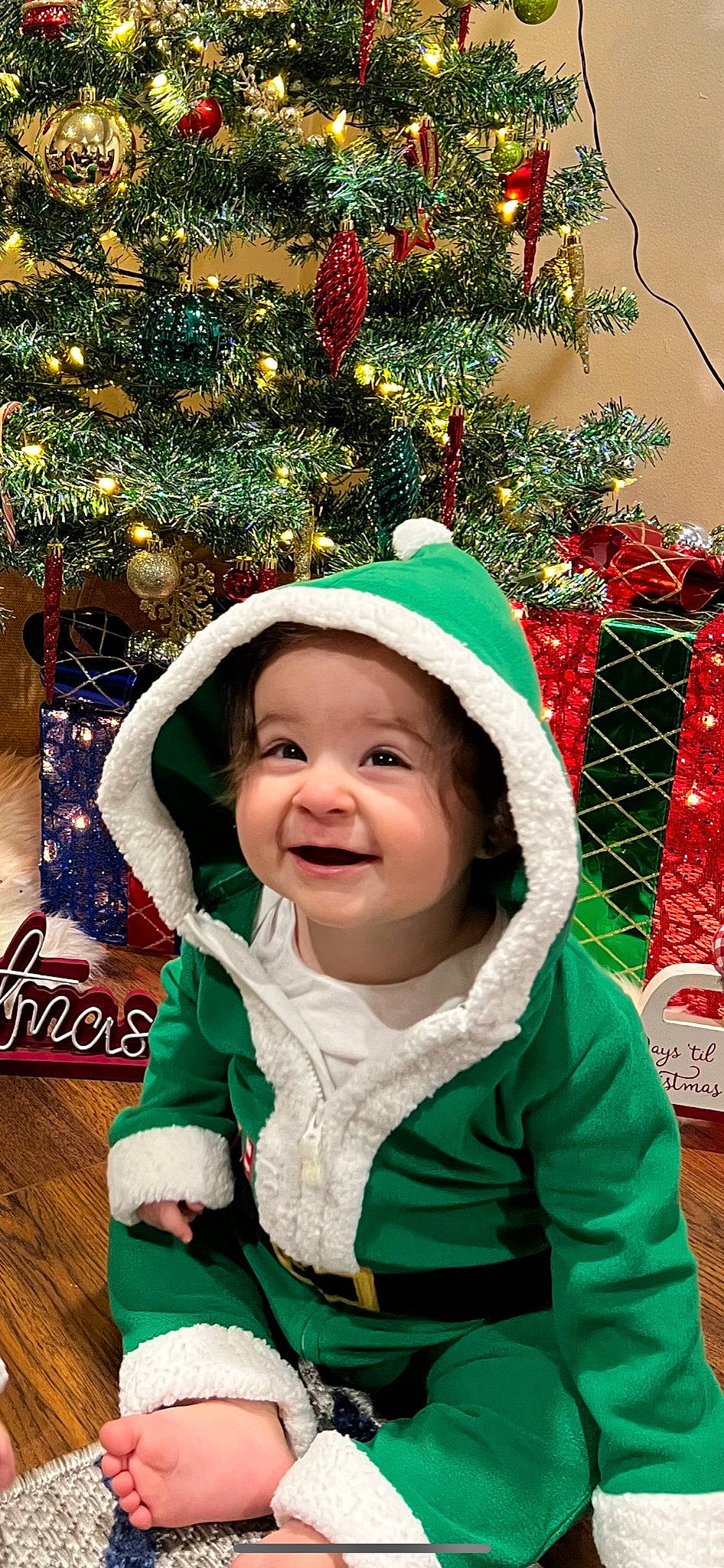 Jenna is registered to the contest to win money with this photo: baby, baby_toddler_clothing, christmas, christmas_decoration, christmas_ornament, christmas_tree, eye, facial_expression, fun, grass, green, happy, head, headwear, holiday_ornament, human_body, jacket, joy, person, smile