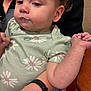 toddler, child, baby, face, arm, hand, food, mouth, clothing, onesie, floral_pattern, person, holding, watch, skin, indoor, table, wood, adult, closeup