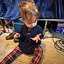 Brailee is registered to the contest to win money with this photo: toddler, child, indoor, carpet, plaid_leggings, navy_sweater, curious, sitting, hand, hair, footwear, box, diapers, floor, cables, background, toy, person, clothing, home