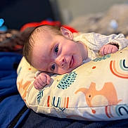 Aurora is registered to the contest to win money with this photo: baby, infant, smile, face, cushion, animal_pattern, rainbow_pattern, blanket, clothing, hand, head, blue, orange, white, cute, portrait, indoors, soft, cozy, child