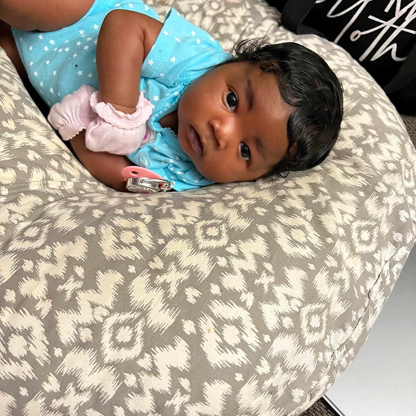 Bella joined the competition — help win amazing prizes! baby, baby_bottle, baby_mittens, blue_onesie, carpet, child, curly_hair, cushion, cute, face, indoor, infant, looking, lying_down, newborn, pacifier, patterned_fabric, person, resting, soft_toys