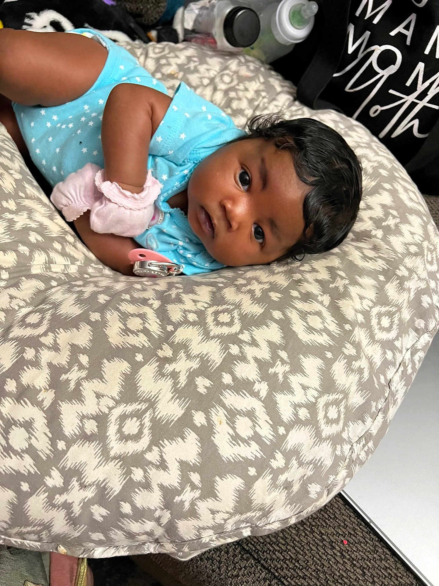 Bella joined the competition — help win amazing prizes! baby, infant, blue_onesie, cushion, patterned_fabric, pacifier, baby_bottle, indoor, carpet, curly_hair, face, looking, lying_down, soft_toys, baby_mittens, child, person, resting, cute, newborn