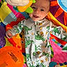 baby, child, dinosaur_pajamas, play_mat, toy, colorful, smiling, infant, lying_down, happy, cute, indoor, bright, clothing, face, person, playtime, fun, young_child, background