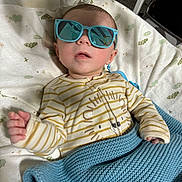 Anthony is registered to the contest to win money with this photo: baby, blanket, child, cozy, cute, face, fashion, hand, head, indoor, infant, knitted_blanket, lion_print, onesie, person, portrait, relaxed, sleepwear, striped_clothing, sunglasses