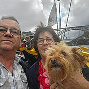 Elsa a rejoint le concours — aidez-le/la à gagner de superbes lots ! couple, dog, boat, selfie, river, bridge, travel, tourism, outdoor, water, portrait, people, glasses, smiling, scruffy_dog, yellow_boat, flag, cityscape, cloudy_sky, vacation