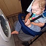 Louis joined the competition — help win amazing prizes! baby, child, pacifier, stroller, kitchen, washing_machine, wooden_cabinet, floor, foot, clothing, seat, baby_carrier, indoor, person, face, hair, hand, holding, sitting, blur