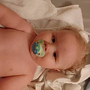 Louis is registered to the contest to win money with this photo: baby, pacifier, towel, blanket, infant, child, skin, face, curly_hair, lying_down, indoors, soft_texture, cute, young_child, portrait, sleepwear, comfort, relaxation, closeup, person