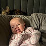 baby, infant, onesie, pink, tongue, smile, cat, tabby, pet, bed, pillow, blanket, cozy, indoor, cute, child, resting, furniture, sleepy, companion