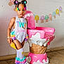 toddler, child, birthday, party, colorful_clothing, hair_accessories, ice_cream_cone, chair, wooden_floor, wall, indoor, portrait, smiling, shoes, socks, decoration, banner, playful, cute, fashion