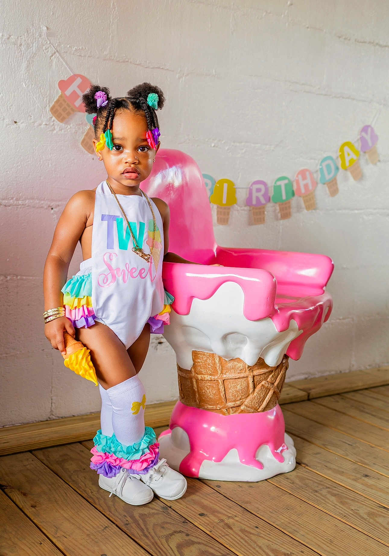 Stori Isabella is registered to the contest to win money with this photo: toddler, child, birthday, party, colorful_clothing, hair_accessories, ice_cream_cone, chair, wooden_floor, wall, indoor, portrait, smiling, shoes, socks, decoration, banner, playful, cute, fashion