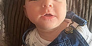 Theo is registered to the contest to win money with this photo: baby, child, denim, overalls, white_shirt, grid_pattern, cushion, texture, close_up, face, eyes, curious, soft_lighting, indoor, portrait, infant, clothing, person, skin, expression