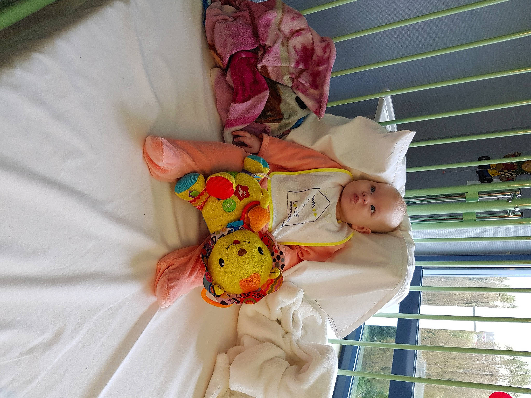 émilia a rejoint le concours — aidez-le/la à gagner de superbes lots ! baby, baby_products, baby_safety, baby_toddler_clothing, baby_toys, child, comfort, facial_expression, fun, hand, happy, human_body, linens, peach, person, pink, room, textile, toddler, toy