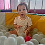 Mia participe au concours pour gagner de l'argent avec cette photo : ball_pit, balls, casual_clothing, child, colorful, curious, cute, decorations, happy, indoor, person, pink_bow, play_area, playful, seated, soft_lighting, toddler, toys, window, young_child