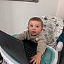 baby, child, high_chair, laptop, sweater, indoor, curious, animal_print, face, hand, technology, furniture, mirror, window_blinds, person, expression, seated, keyboard, candid, home