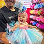 Ember is registered to the contest to win money with this photo: baby, man, tutu, headband, smile, beard, cap, clothing, colorful, retail, display, fabric, happy, person, indoor, shopping, dress, holding, tulle, cute
