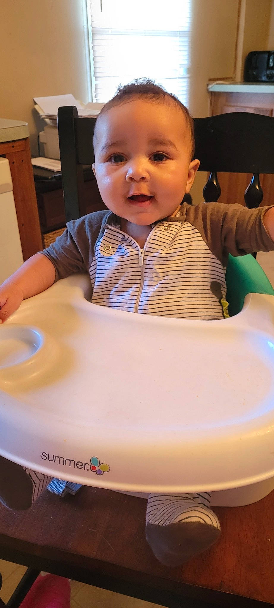 Zayden is registered to the contest to win money with this photo: automotive_wheel_system, baby, baby_toddler_clothing, bib, chair, cheek, child, chin, face, facial_expression, fun, head, leisure, person, sitting, skin, smile, t_shirt, table, thumb