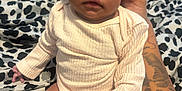 Sylea is registered to the contest to win money with this photo: baby, infant, child, person, white_clothing, tattoo, hand, blanket, patterned_blanket, sitting, skin, curly_hair, indoors, cute, young_child, portrait, expression, supporting_hand, close_up, soft_lighting