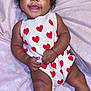 baby, blanket, child, comfort, curly_hair, cute, hands, happy, heart_pattern, indoors, infant, legs, lying_down, playful, portrait, red_bows, skin, smiling, soft_texture, white_outfit