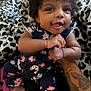 baby, child, curly_hair, smiling, tattoo, hand, arm, bed, blanket, pattern, floral_clothing, infant, happy, indoors, person, cute, skin, foot, playful, holding
