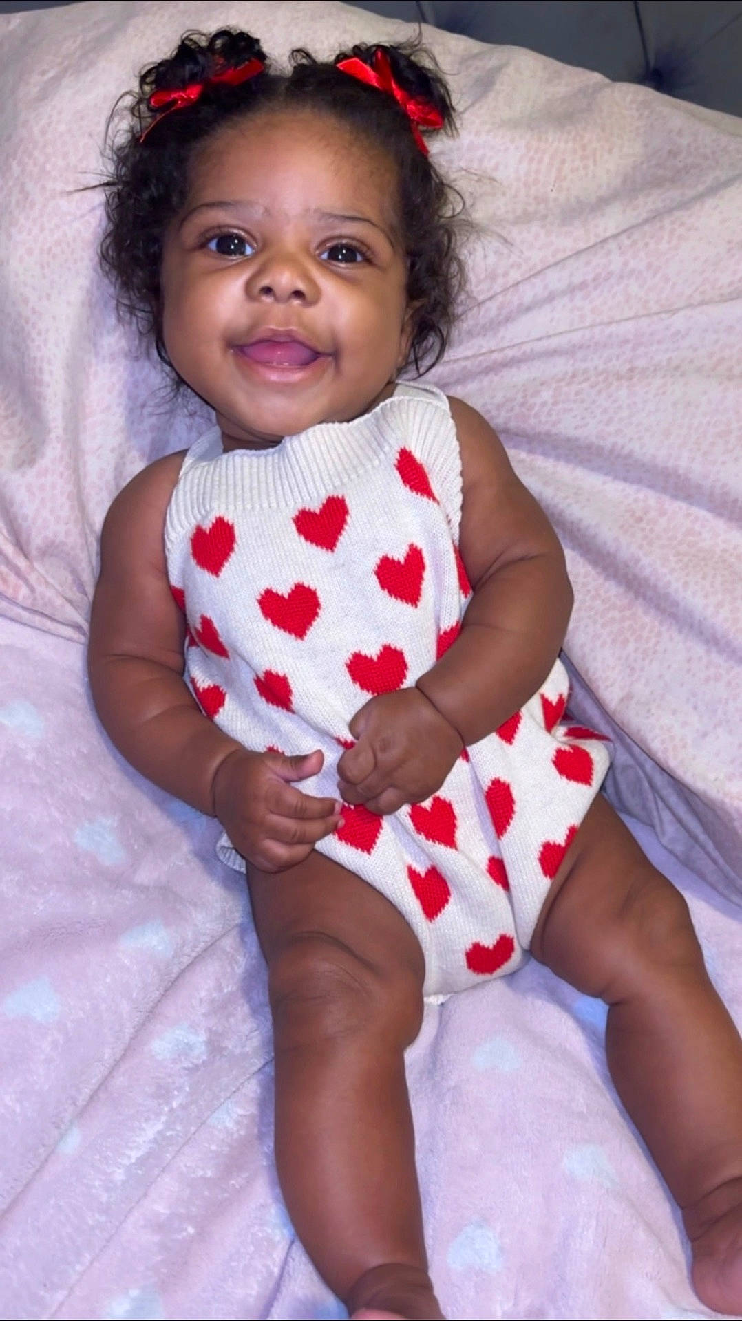 baby, blanket, child, comfort, curly_hair, cute, hands, happy, heart_pattern, indoors, infant, legs, lying_down, playful, portrait, red_bows, skin, smiling, soft_texture, white_outfit