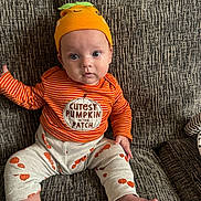 Jenson joined the competition — help win amazing prizes! baby, child, infant, orange_hat, striped_shirt, pumpkin_outfit, cute, sitting, couch, home_interior, face, foot, hand, expression, text_on_clothing, patterned_pants, cozy, indoors, young_child, portrait