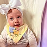 Shayla joined the competition — help win amazing prizes! baby, infant, child, portrait, smiling, happy, face, eyes, white_bow, headband, bib, duckling, clothing, sleeves, quilted_blanket, indoor, close_up, sitting, nursery, photograph