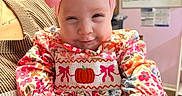 Shayla joined the competition — help win amazing prizes! baby, child, infant, smiling, portrait, pink_bow, floral_dress, pumpkin, seated, chair, indoor, close_up, face, eyes, happy, colorful_clothing, cozy, hospital_room, background_sign, photography