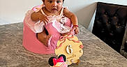 Aylany is registered to the contest to win money with this photo: baby, infant, pink_outfit, pink_seat, cupcake, minnie_mouse, table, marble, wooden_sign, 6_months, celebration, child, face, hair_clip, sitting, curious, indoor, chair, black_chair, decor