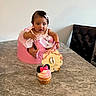 baby, infant, pink_outfit, pink_seat, cupcake, minnie_mouse, table, marble, wooden_sign, 6_months, celebration, child, face, hair_clip, sitting, curious, indoor, chair, black_chair, decor