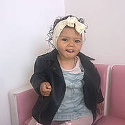Branda Devert participe au concours pour gagner de l'argent avec cette photo : bow, child, curly_hair, cute, denim_dress, fashion, footwear, headband, indoor, leather_jacket, leggings, light_background, person, pink_chair, playful_expression, portrait, sitting, smile, toddler, young_child