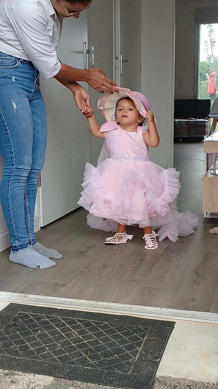 Branda Devert a rejoint le concours — aidez-le/la à gagner de superbes lots ! adult_hand, carpet, chair, child, cute, door, flooring, footwear, hat, helping_hand, home_interior, indoor, jeans, learning_to_walk, person, pink_dress, socks, table, toddler, window