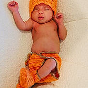 Eithan Milan is registered to the contest to win money with this photo: baby, booties, child, cozy, cute, diaper_cover, face, hand, indoors, infant, knitted_clothing, newborn, orange_hat, peaceful, portrait, relaxed, resting, sleeping, soft_surface, warm_colors