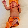 baby, booties, child, cozy, cute, diaper_cover, face, hand, indoors, infant, knitted_clothing, newborn, orange_hat, peaceful, portrait, relaxed, resting, sleeping, soft_surface, warm_colors