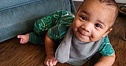 Legend is registered to the contest to win money with this photo: baby, bib, child, crawling, cute, face, floor, furniture, green_clothing, happy, home, indoor, infant, onesie, person, plug, smiling, sofa, wall_socket, wooden_floor