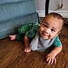 baby, bib, child, crawling, cute, face, floor, furniture, green_clothing, happy, home, indoor, infant, onesie, person, plug, smiling, sofa, wall_socket, wooden_floor