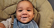 Legend is registered to the contest to win money with this photo: baby, bib, cheerful, child, clothing, cute, face, feeding, food, happy, high_chair, indoor, infant, messy, person, portrait, seatbelt, smile, toddler, young