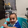 Legend is registered to the contest to win money with this photo: baby, child, infant, smiling, happy, portrait, indoor, laundry_basket, turquoise, blue_clothing, bib, sitting, carpet, bedroom, dresser, storage_bins, curtains, suitcase, straw_hat, home