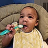 Legend is registered to the contest to win money with this photo: baby, bib, child, clothing, cute, dinnertime, expression, face, feeding, food, hand, high_chair, indoor, infant, kitchen, meal_time, seat, spoon, table, young_child
