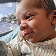 Legend is registered to the contest to win money with this photo: baby, infant, face, smile, clothing, onesie, skin, head, cute, portrait, newborn, child, baby_garment, expression, indoors, person, young_child, soft_lighting, closeup, sleepwear