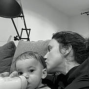 Andrea a rejoint le concours — aidez-le/la à gagner de superbes lots ! adult, black_and_white, blanket, bottle, ceiling, child, couch, cozy, cuddle, face, feeding, hair, indoor, kiss, lamp, living_room, parent, portrait, profile, sofa